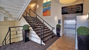 Un escalier avec une rampe, une enseigne indiquant « FRASER HOUSE », et un tableau accroché au mur.