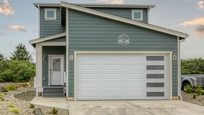 A two-story house with a garage, a front porch, and a small deck. - The Sanctuary - Oyhut Bay Seaside Village (Ocean Shores)
