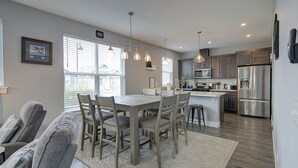 A modern kitchen with a central island, stainless steel appliances, and a dining area with a light-colored rug. - The Sanctuary - Oyhut Bay Seaside Village (Ocean Shores)