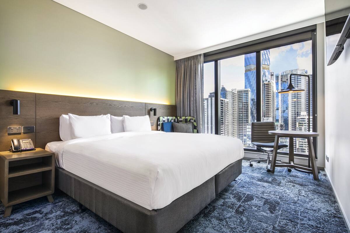 Una habitación de hotel con una cama grande, un escritorio, una silla y vistas a edificios altos.