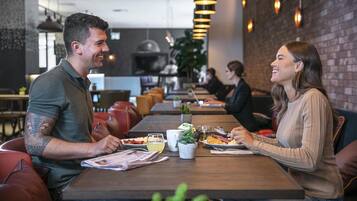 Restaurante com mesas e cadeiras de madeira, parede de tijolos e luminárias pendentes.