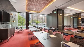 A modern conference room with a large table, chairs, a TV, and a city view through large windows.