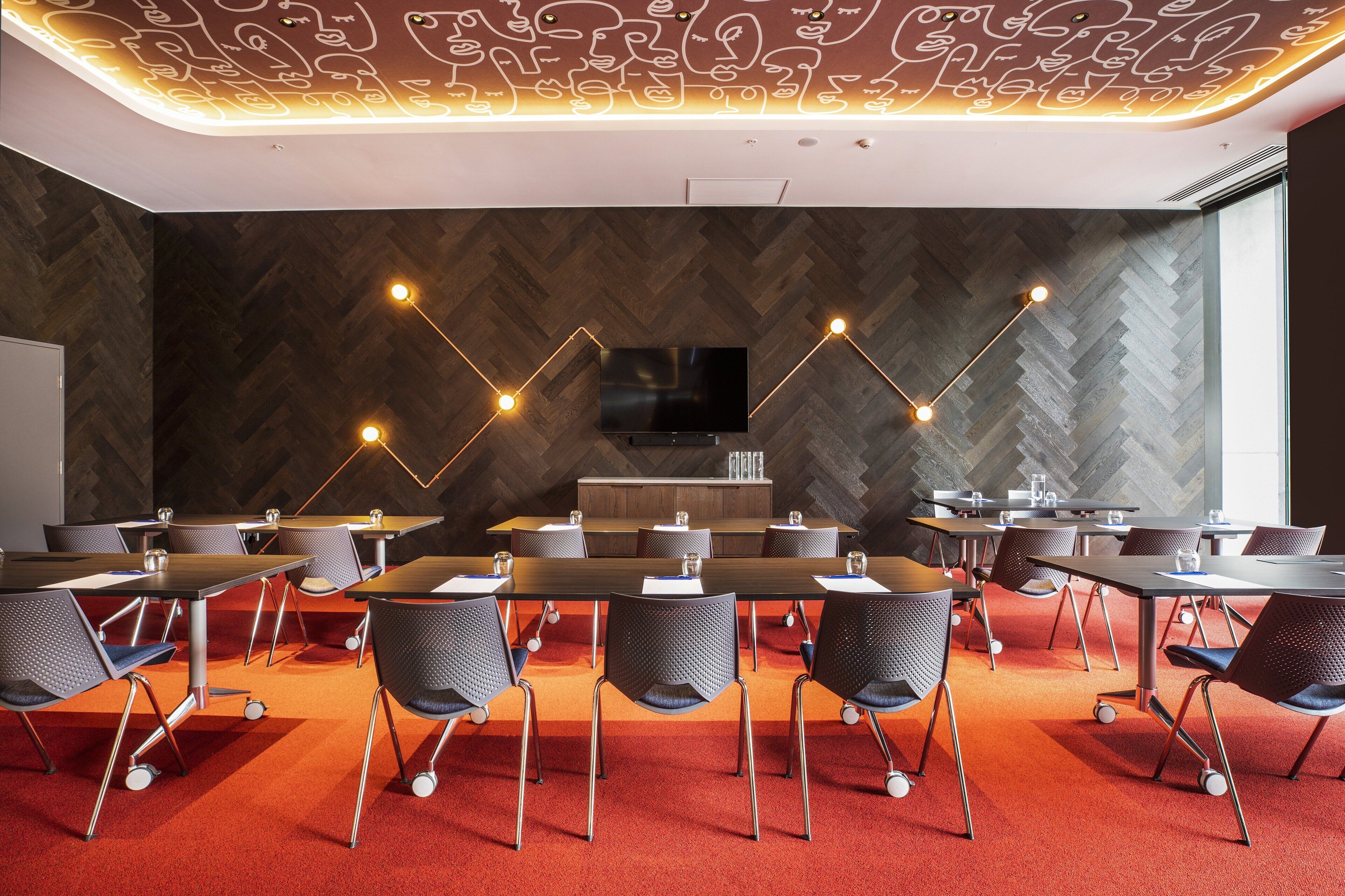 A conference room with a herringbone-patterned wall, a flat-screen TV, and a modern chandelier.
