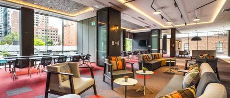 A modern lounge area with seating arrangements, tables, and a large window offering a city view.