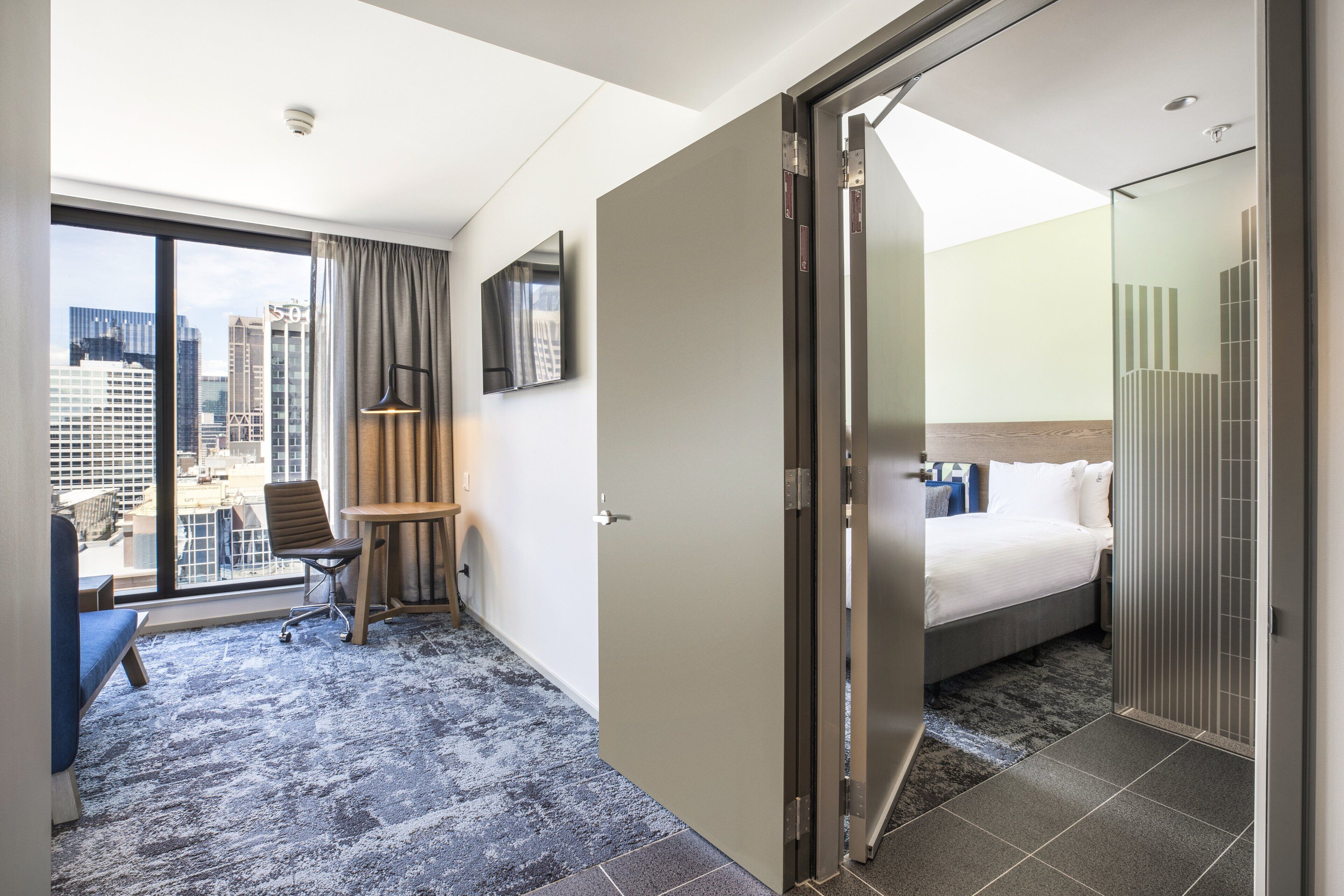 A hotel room with a bed, a desk, a chair, a TV, and a city view.