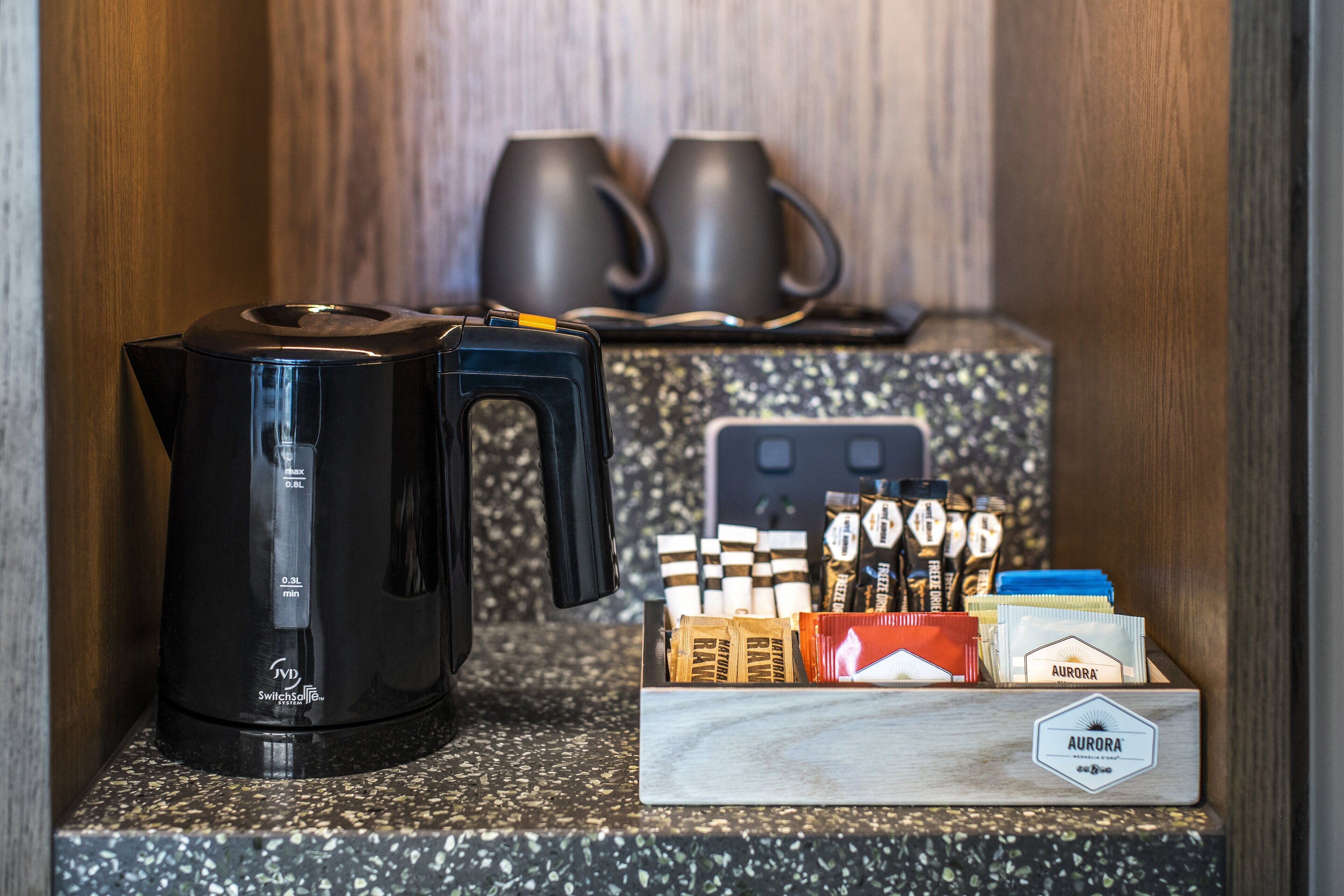 Une machine à café, deux tasses et une boîte de capsules de café sont posés sur un plan de travail.