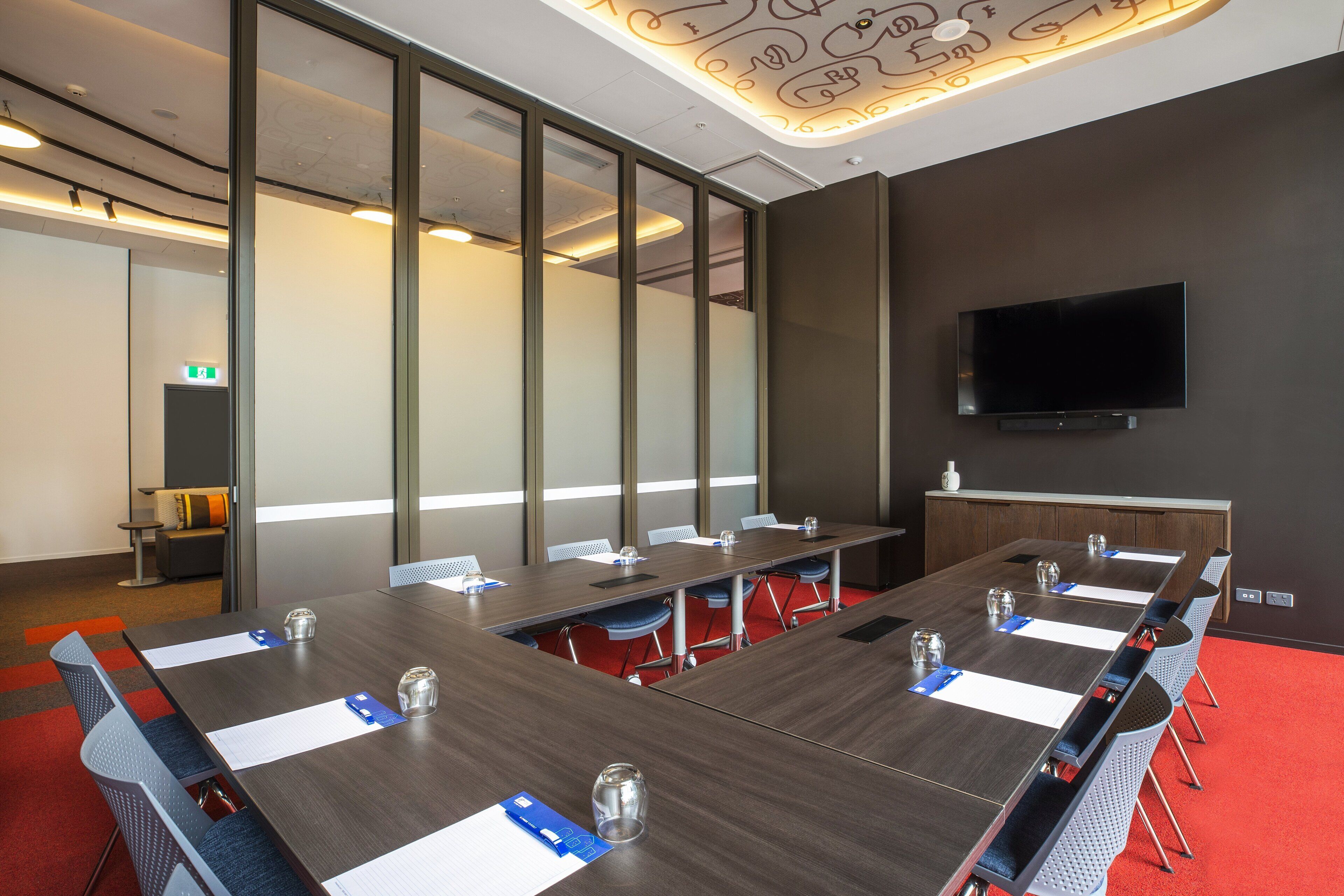 A conference room with a long table, chairs, and a TV on the wall.