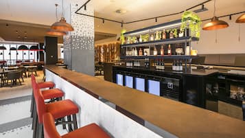 A modern bar area with a long counter, red bar stools, and a variety of liquor bottles displayed on shelves.