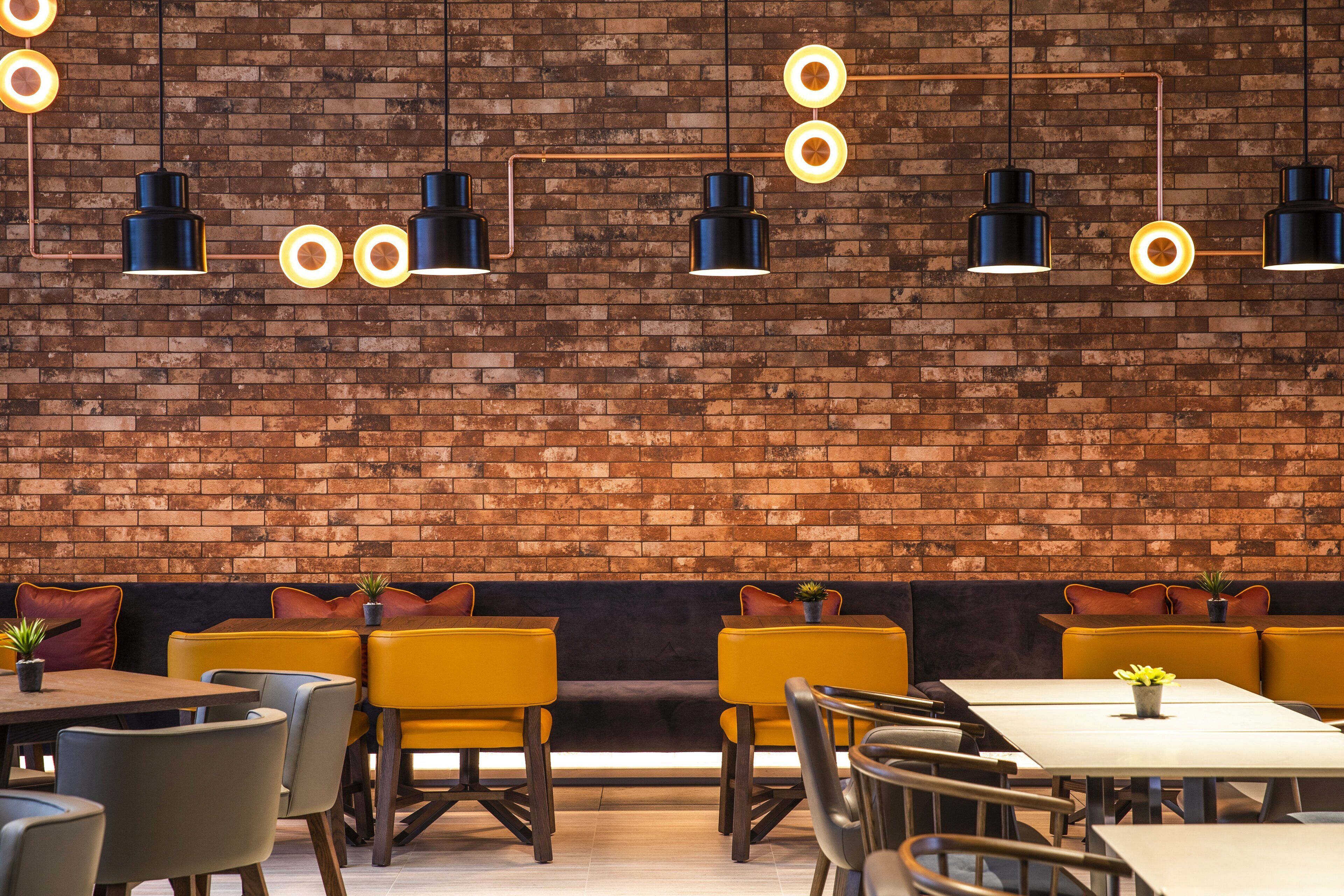 Ein Restaurant mit Ziegelwänden, gelben Sitzgruppen und schwarzen Pendelleuchten.