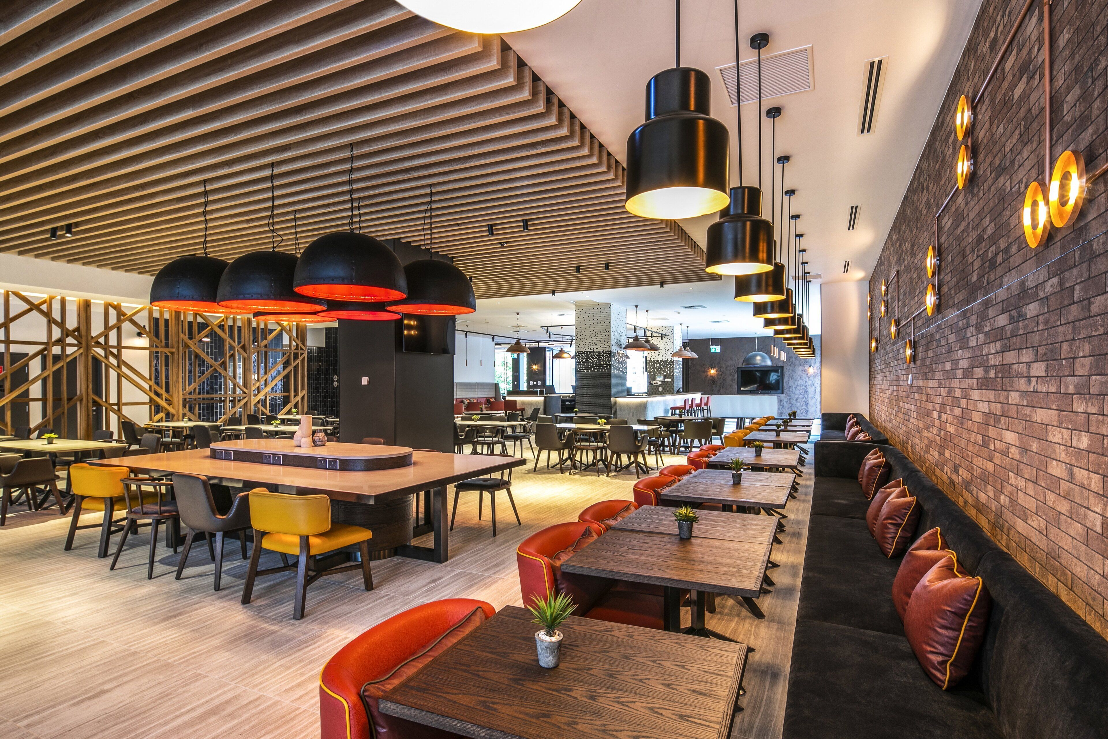 Un restaurante moderno con paneles de techo de madera, luces colgantes negras y una pared de ladrillo.