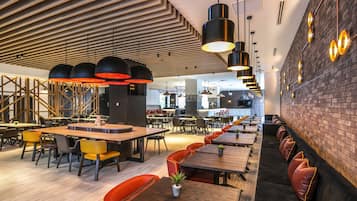 Un restaurante moderno con paneles de techo de madera, luces colgantes negras y una pared de ladrillo.