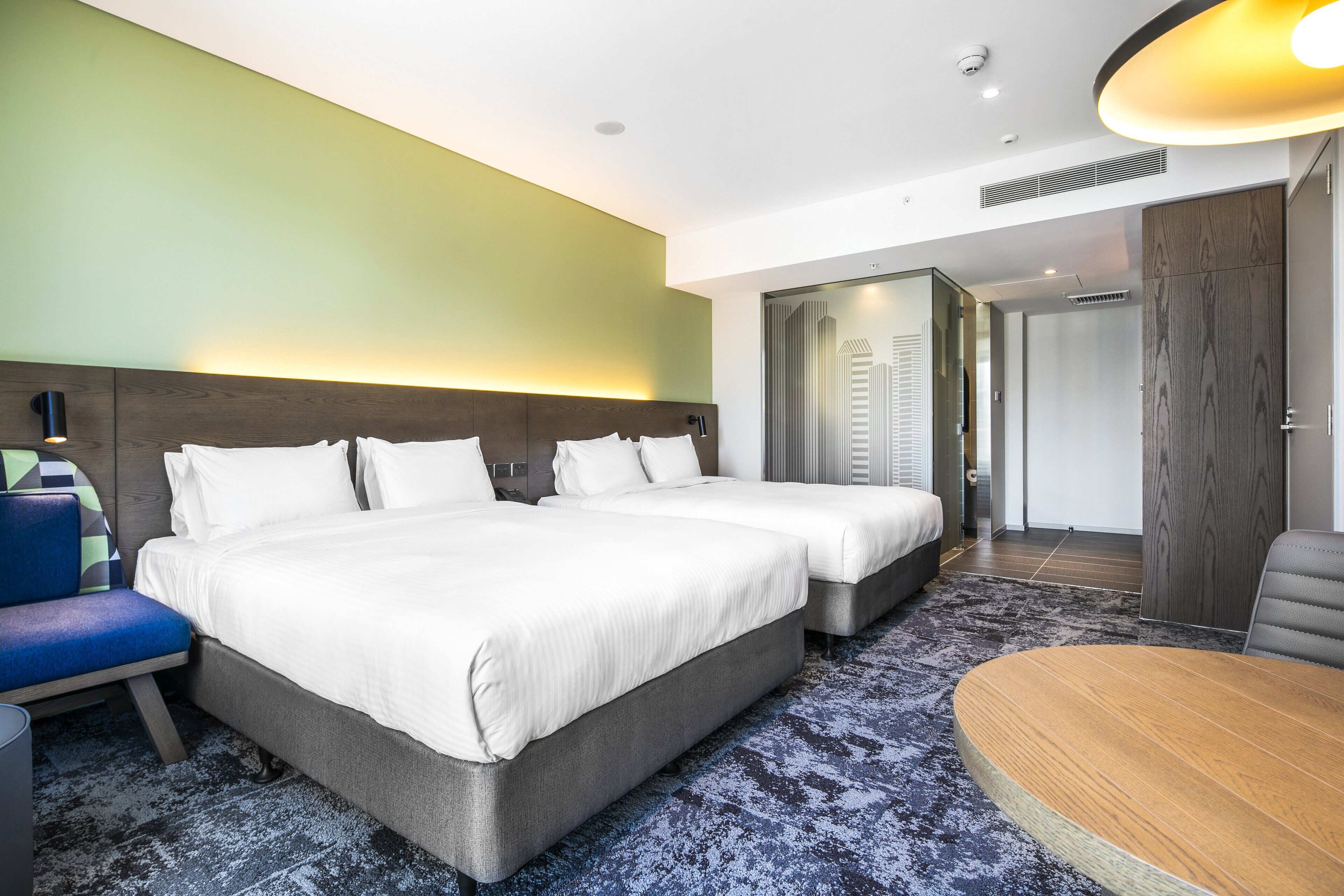 A hotel room with two beds, a desk, a chair, and a view of the city skyline.