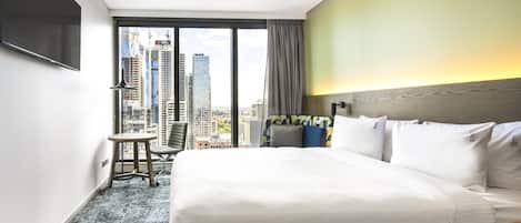 Habitación de hotel con una cama grande, un escritorio, una silla y vistas a la ciudad a través de la ventana.