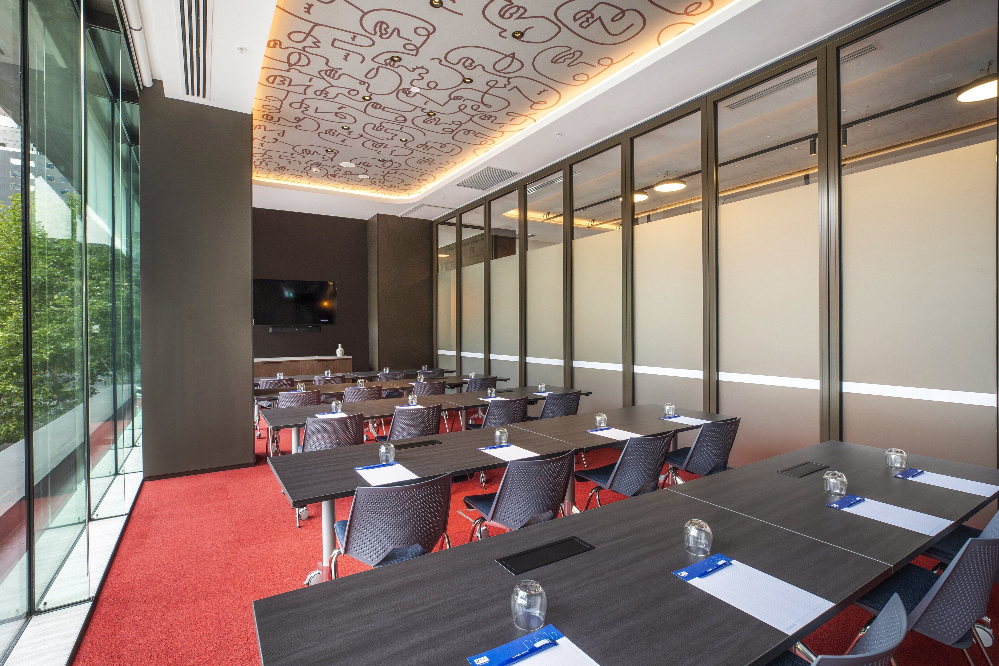 Un salón de conferencias con varias mesas, sillas y una pantalla grande.
