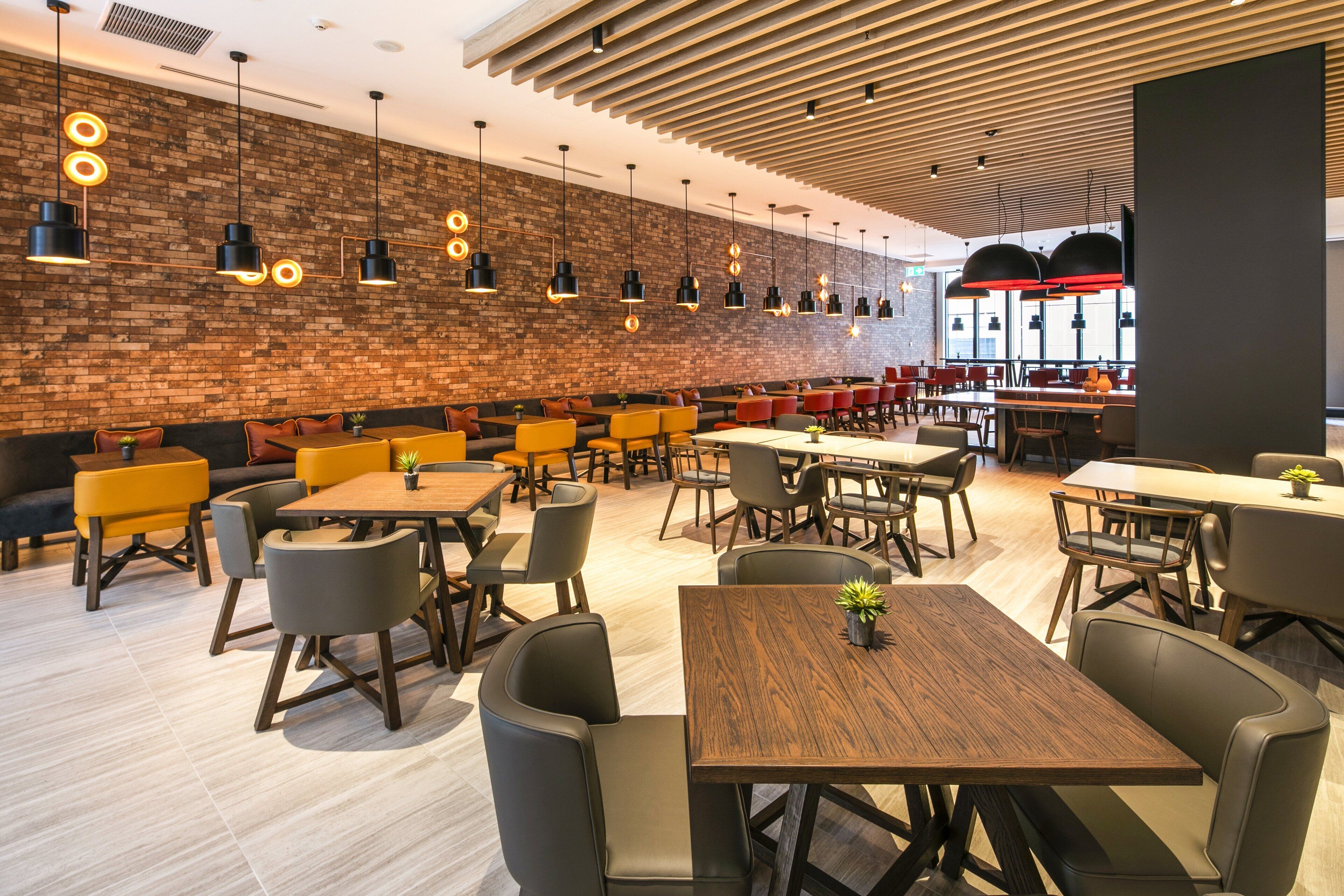 A modern restaurant with wooden tables and chairs, brick walls, and pendant lighting.