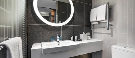 A modern bathroom with a large mirror, white sink, and a towel rack.