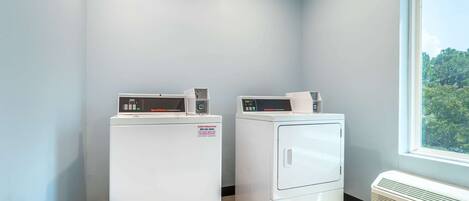 A laundry room with two front-loading washing machines and a wall-mounted heater.