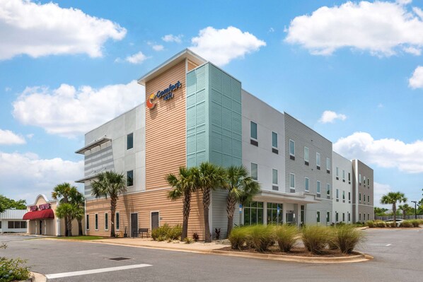 A Comfort Inn hotel with a modern design, featuring a mix of wood and metal siding, multiple windows, and a parking lot with palm trees.