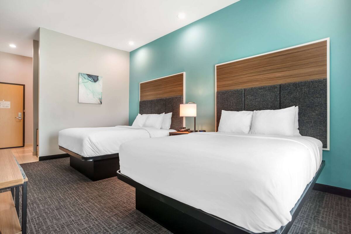 A hotel room with two beds, a desk, and a door.