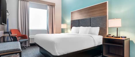 A hotel room with a large bed, a desk, a chair, a TV, and a nightstand with a lamp.