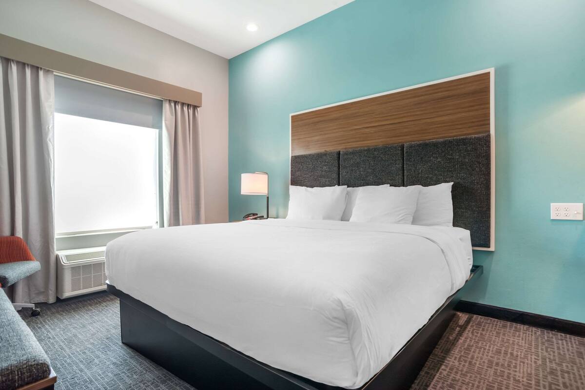 A hotel room with a large bed, a nightstand, a lamp, and a window with curtains.