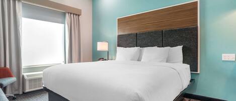 Ein Hotelzimmer mit einem großen Bett, einem Nachttisch, einer Lampe und einem Fenster mit Vorhängen.