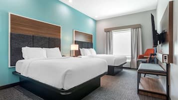 A hotel room with two beds, a TV mounted on the wall, a small table, and a window with curtains.