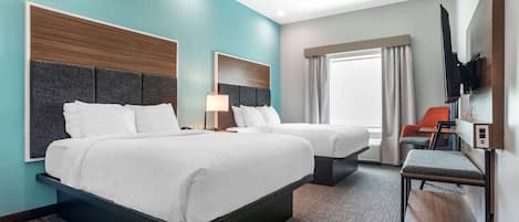 Habitación de hotel con dos camas, un televisor montado en la pared, una mesita y una ventana con cortinas.