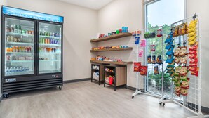 A clean, modern room with a large window, a refrigerator stocked with beverages, a snack display, and a small desk area. - Comfort Inn Miramar Beach-Destin (Miramar Beach)