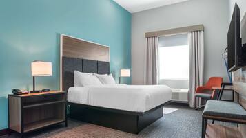 Habitación de hotel con cama, mesitas de noche, escritorio, silla, televisor y ventana con cortinas.
