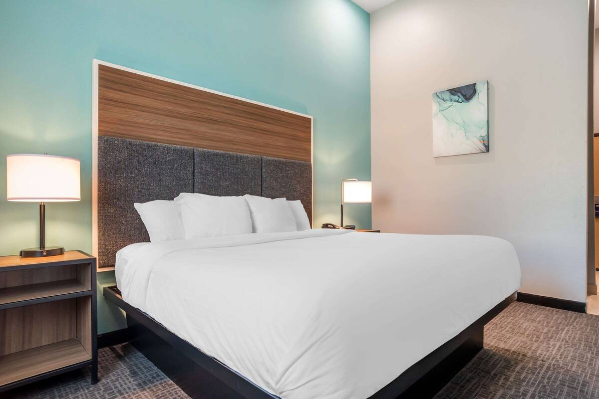 A neatly made bed with white linens, a grey headboard, and two bedside lamps.