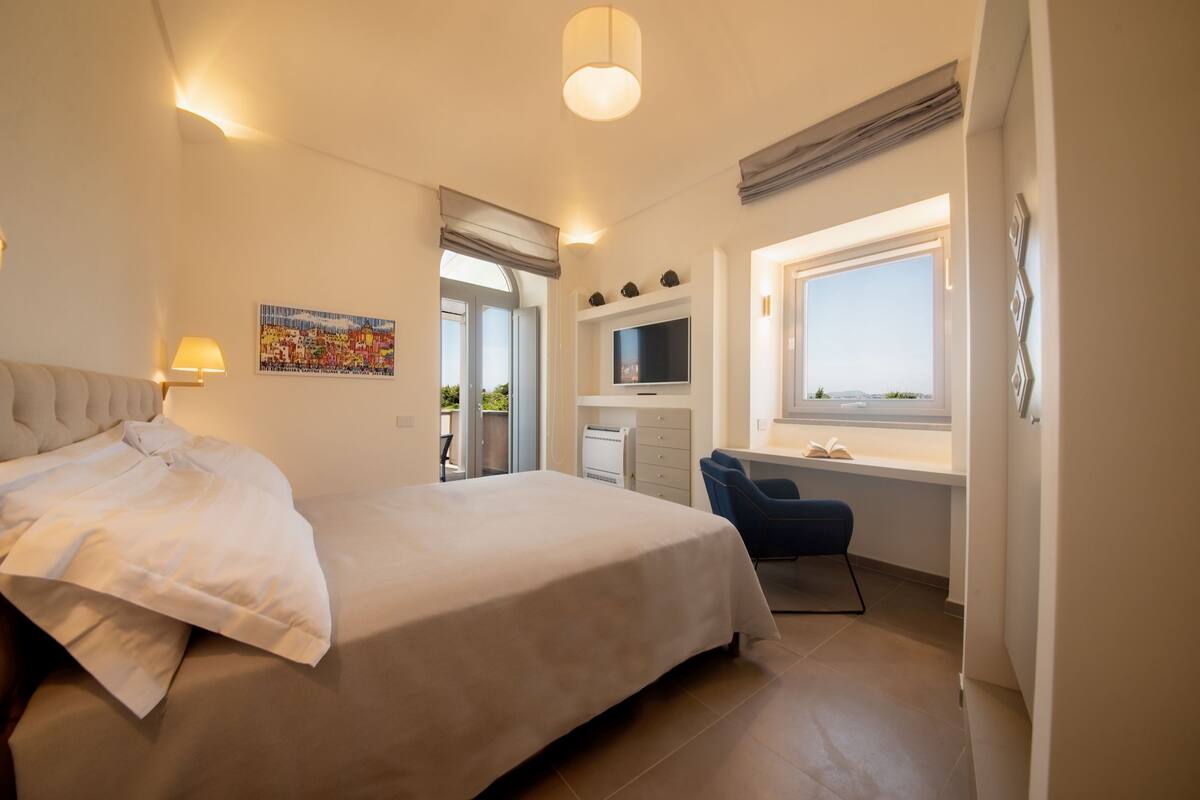 Un dormitorio con cama, un escritorio con silla, televisor y ventana con vistas.