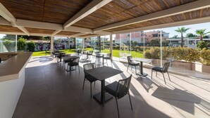 Un espace de restauration extérieur abrité, doté de plusieurs tables et chaises, d’un comptoir et offrant une vue sur une pelouse verdoyante et des bâtiments en arrière-plan.