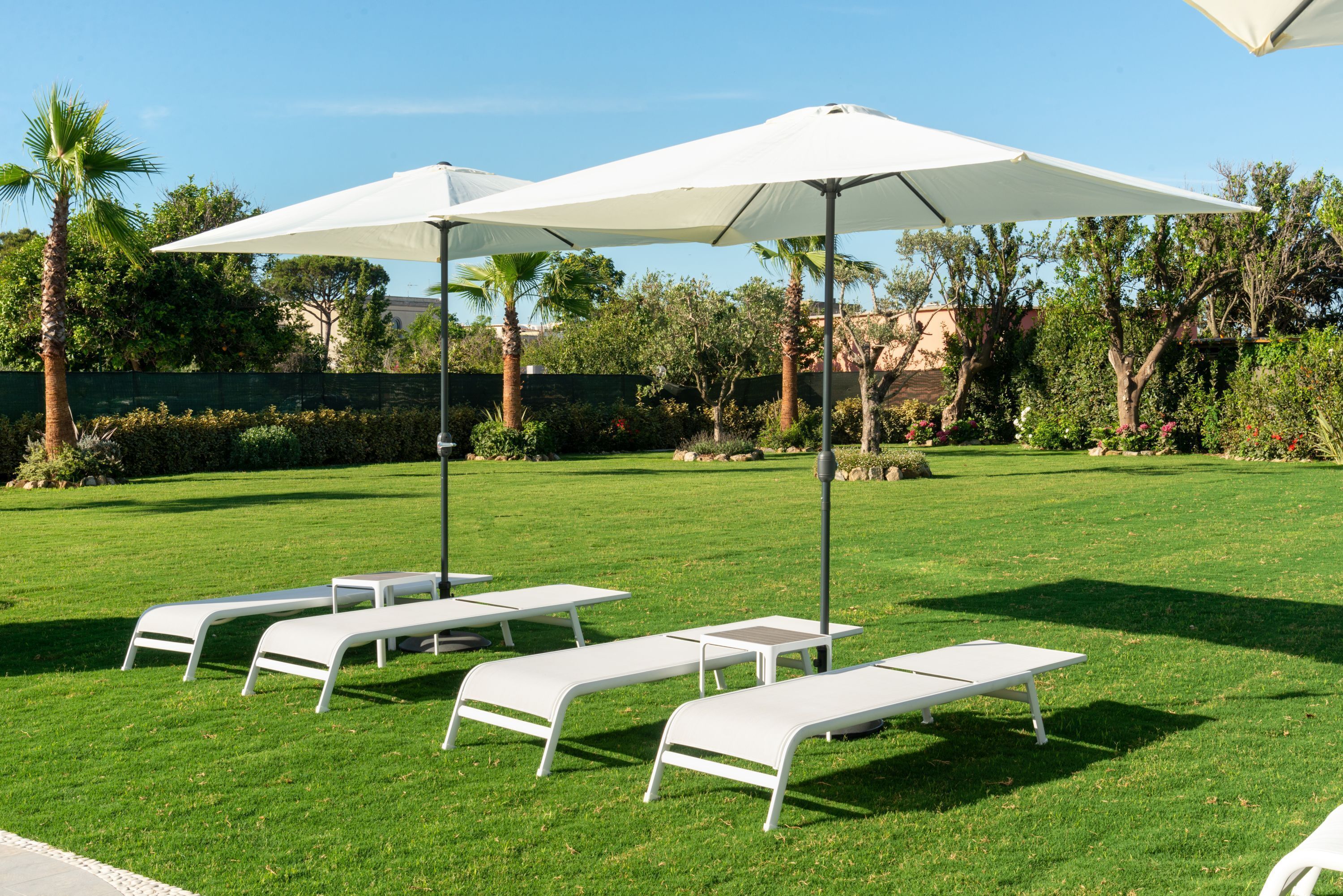 Un espace extérieur bien entretenu, agrémenté de chaises longues blanches et de parasols, entouré d’une végétation luxuriante et d’arbres.