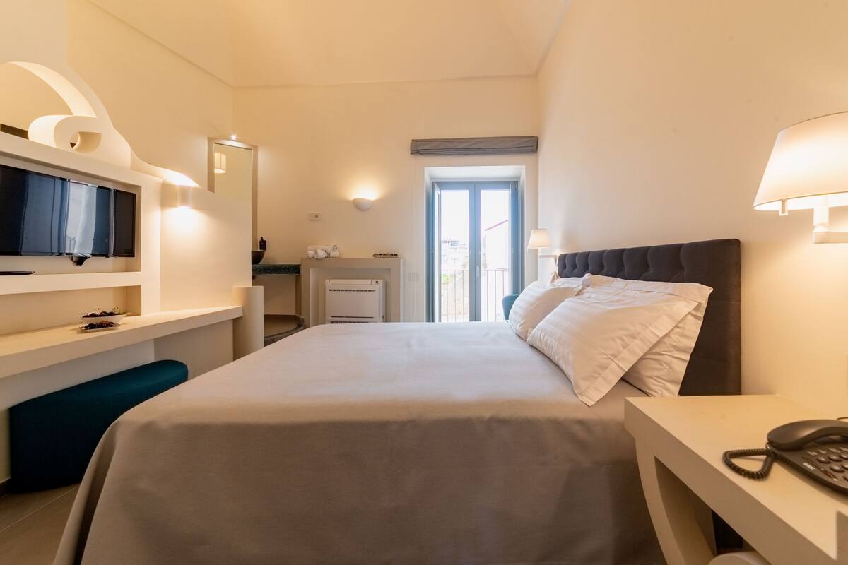 Una habitación de hotel con cama, mesita de noche, televisión y escritorio con silla.