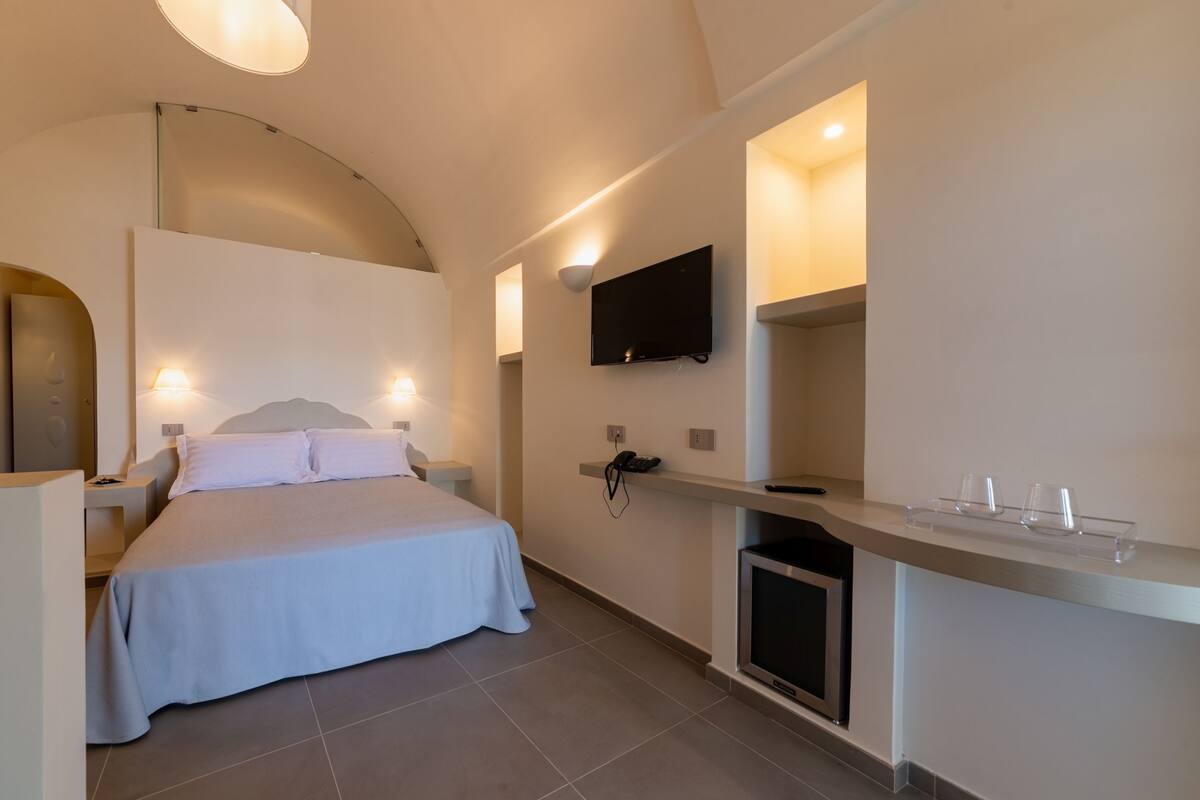 Habitación de hotel moderna con cama, mesitas de noche, televisor de pantalla plana y un televisor pequeño sobre un soporte.