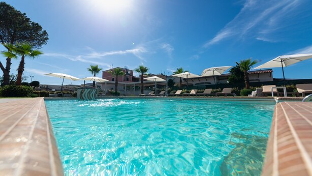 Une piscine entourée de palmiers et d’immeubles, avec des chaises longues et des parasols.