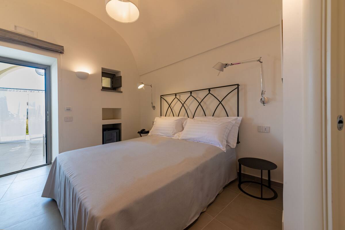 Un dormitorio moderno con una cama grande, una mesita pequeña y una lámpara en el techo.
