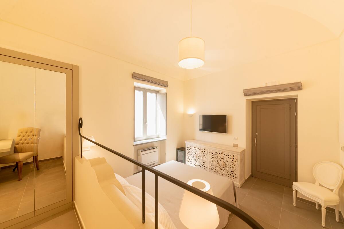 Un dormitorio con cama, televisión en la pared, ventana, puerta y una silla.