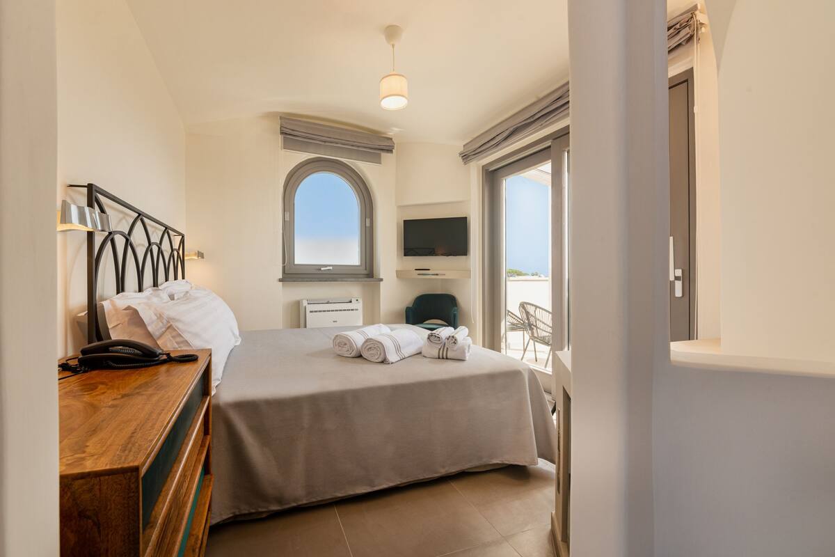 Habitación de hotel con cama, escritorio con teléfono, televisión y ventana con vistas.
