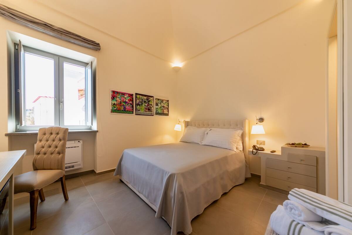 Un dormitorio con una cama, una silla, un escritorio y una ventana.