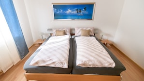 Una cama doble con estructura de madera, dos mesitas de noche con lámparas, y un cuadro de una playa tropical sobre la cama.