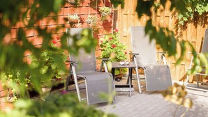 Un patio con dos sillas de metal y una mesa, rodeado de plantas en macetas y una valla de madera.