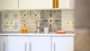 Una cocina con armarios blancos, un salpicadero estampado y un taburete de madera.