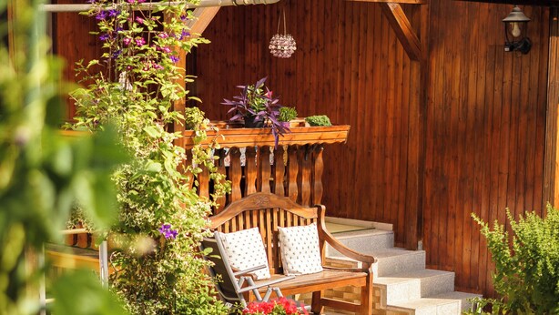 Un banco de madera con un jardinero, una cerca de madera y una zona de jardín con diversas plantas.