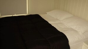 Una cama con edredón blanco y negro, una almohada blanca y una pared lisa con líneas verticales.