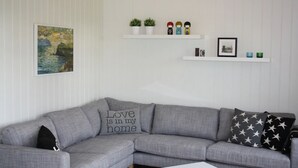 Una sala de estar moderna con un sofá seccional gris, un cuadro de un paisaje enmarco y estantes decorativos con plantas y figuritas.