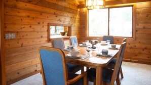 Un intérieur en bois avec une table à manger dressée pour six personnes, entourée de chaises, et une grande fenêtre laissant entrer la lumière naturelle.