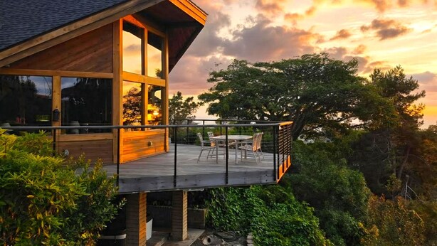 Une maison moderne dotée d’un balcon, de grandes fenêtres et offrant une vue sur les arbres.