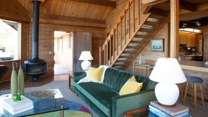 Un intérieur chaleureux en bois, avec un canapé vert, une cheminée, un escalier et un coin cuisine.